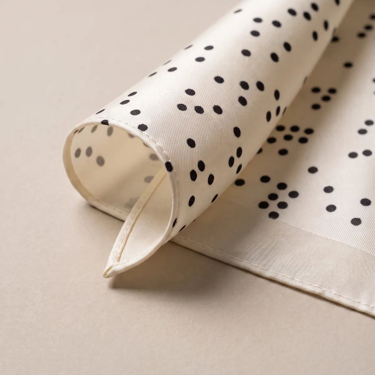 Corner of the dotted silk scarf curled over, showing the narrow cream hem and clusters of black dots