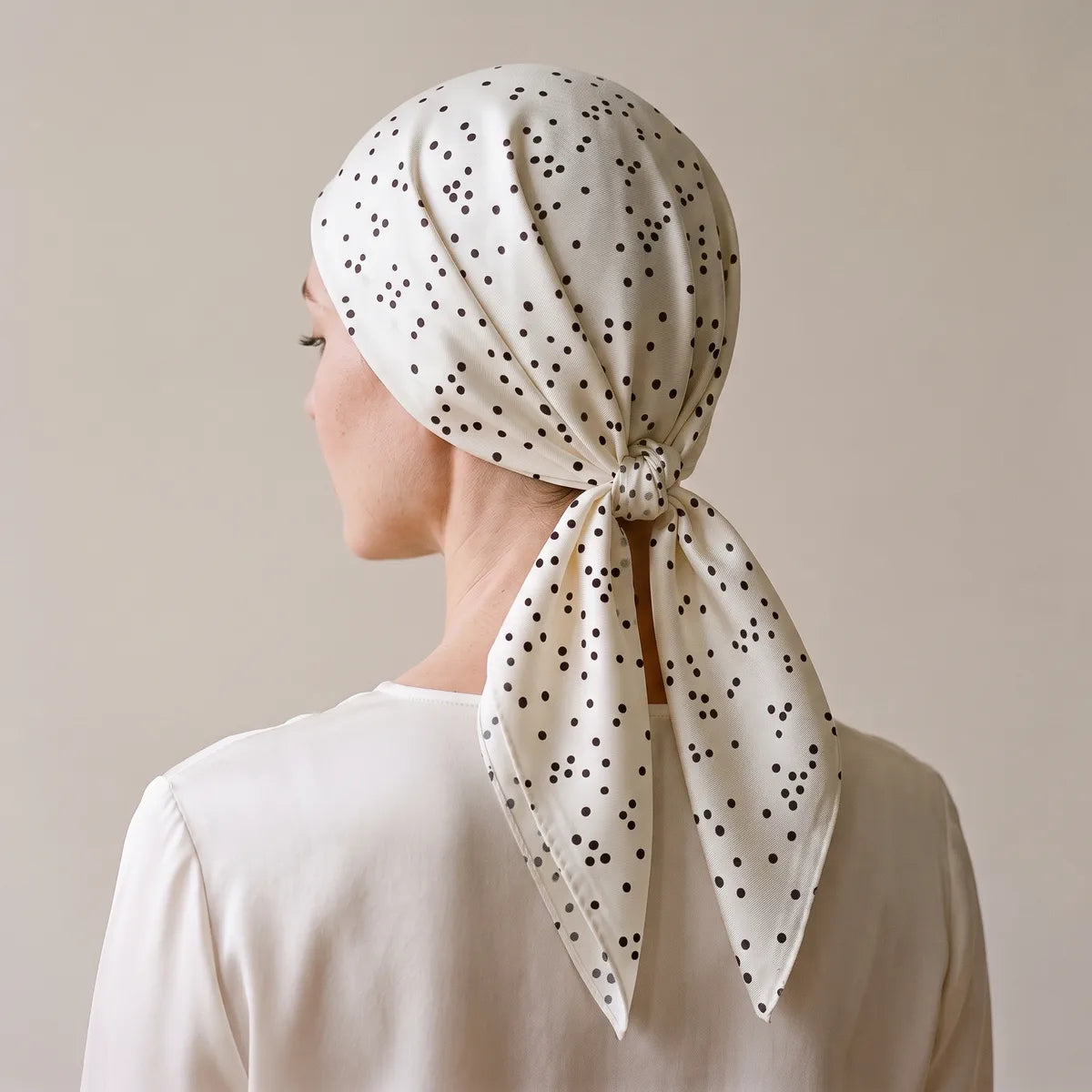 Polka dot silk square worn over the hair and knotted at the nape, seen from behind