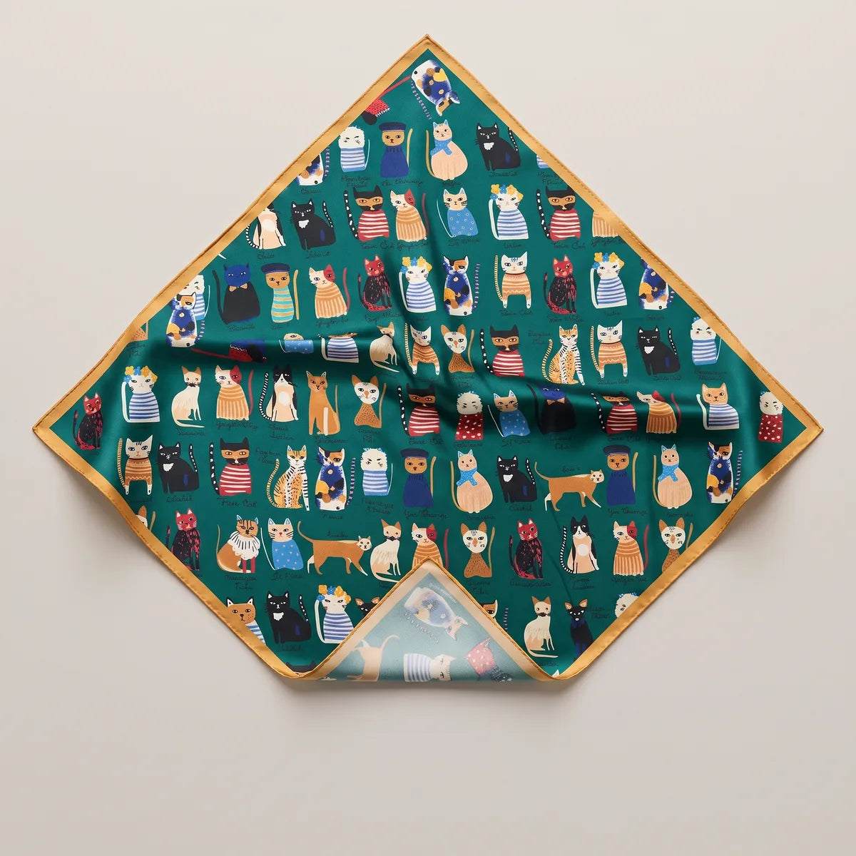 Green cat print silk bandana on its point, rows of cats in striped sweaters within a mustard edge