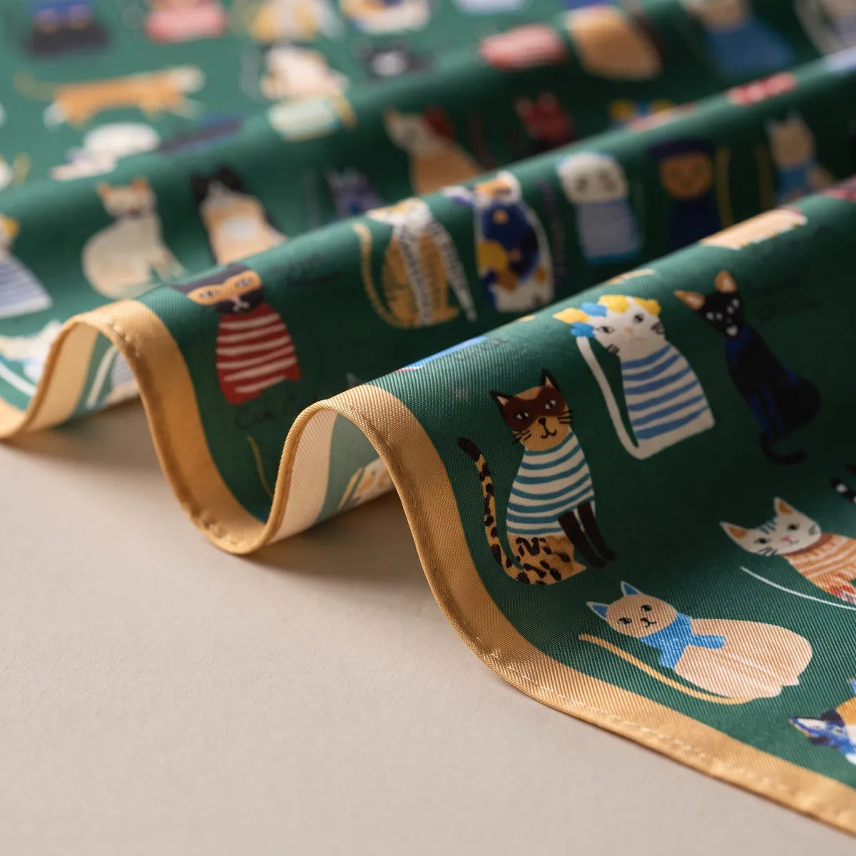 Loose folds of green silk with cats in striped sweaters and a mustard hem along the wavy edge