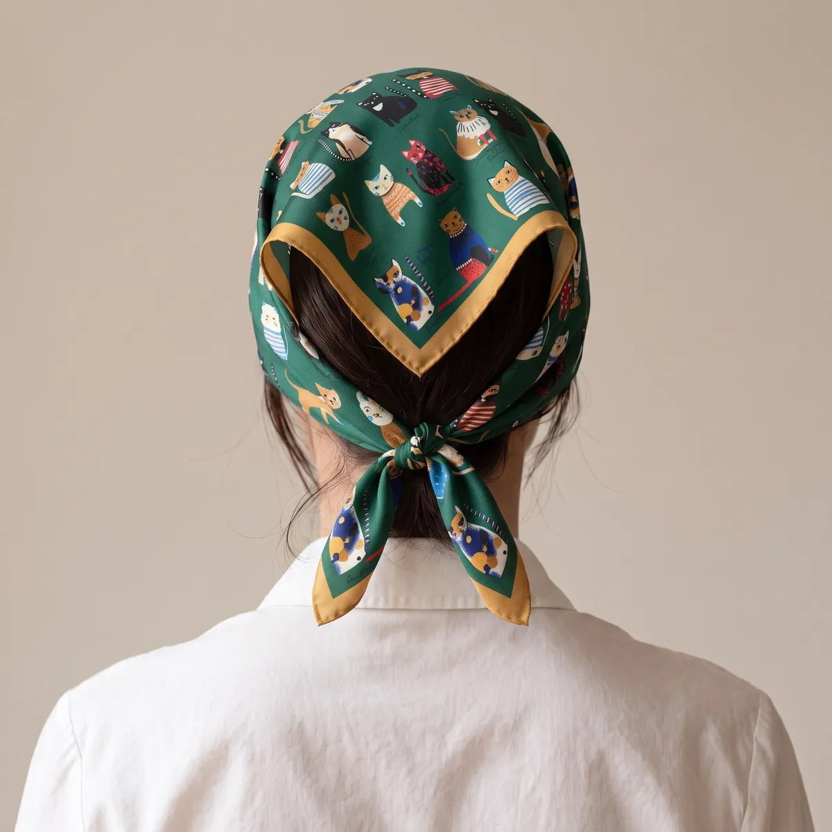 Back view of the cat print silk bandana covering the hair, its mustard border pointing down to the nape knot