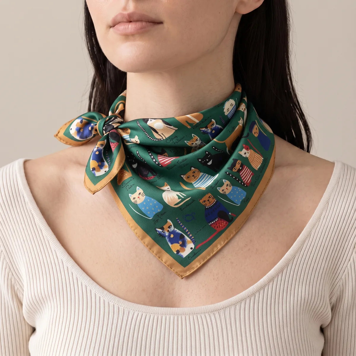 Green cat bandana worn at the neck with a side knot, the point resting on a cream ribbed top