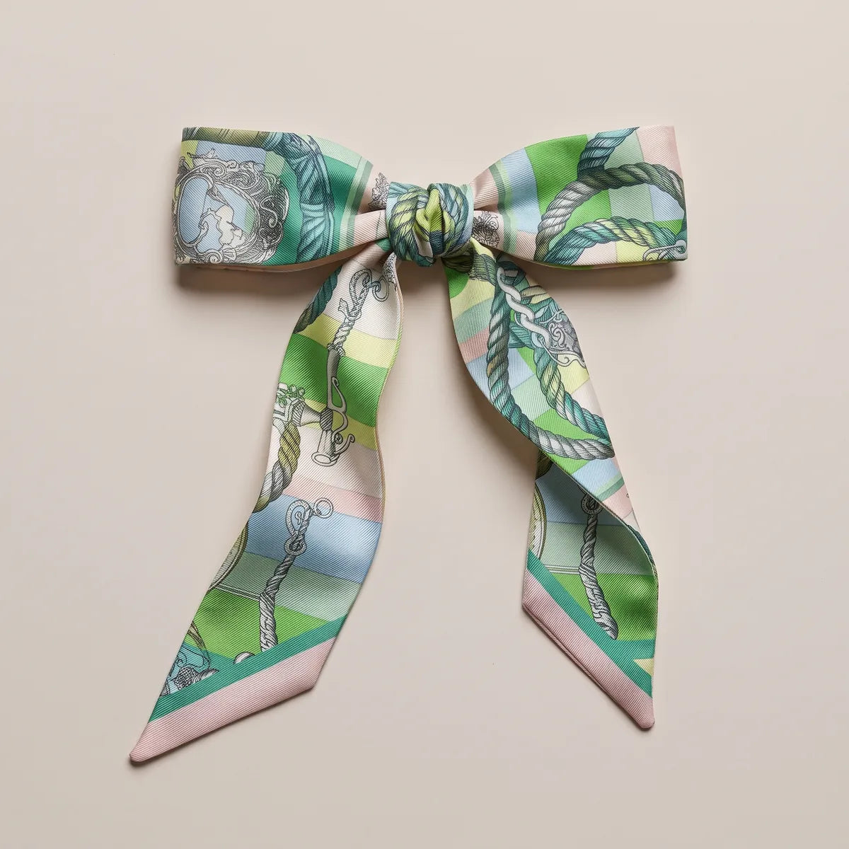 Pastel green skinny silk scarf tied in a bow, an oval crest and twisted rope on the loops