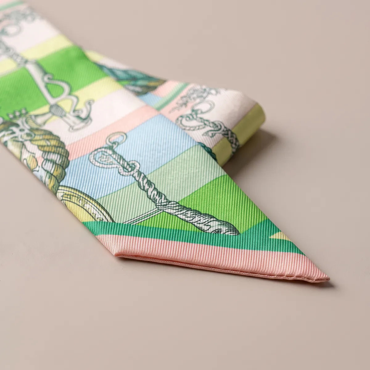 Blush pink tip of the green skinny scarf, a twisted handle with a ring over green and powder blue bands