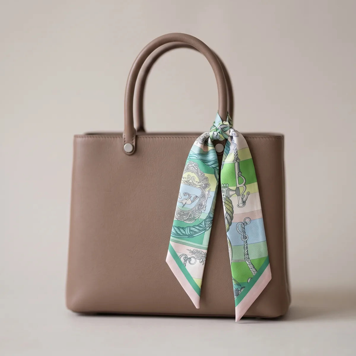 Green chain print skinny silk scarf hanging from a taupe bag handle