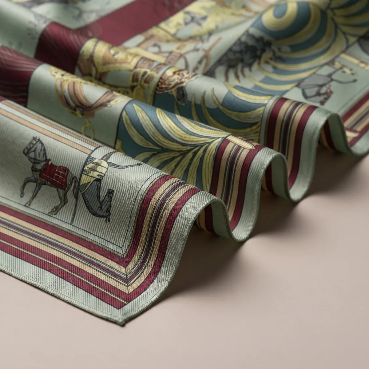 Folds of the sage green scarf showing a small horse in a red blanket and burgundy and cream stripes