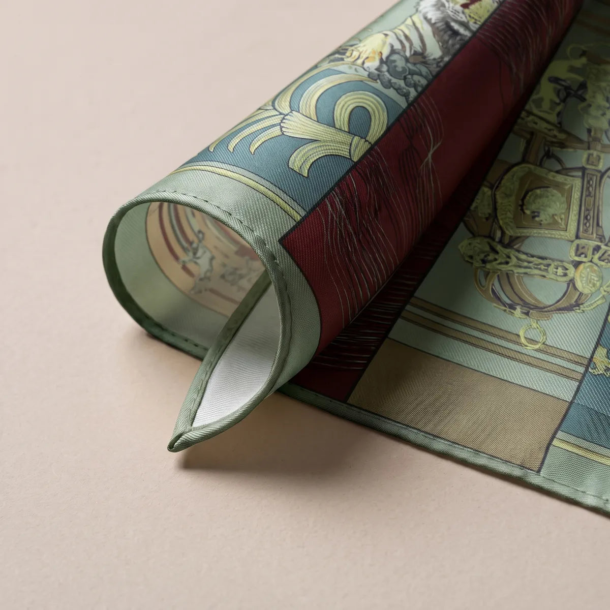 Sage-edged corner of the equestrian silk scarf rolled over to show the pale reverse