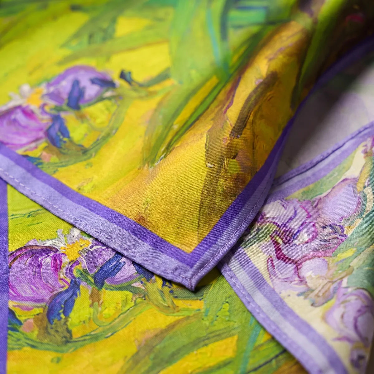 Close-up corner of the painted iris silk scarf: yellow ground, violet petals and the two-tone lilac border