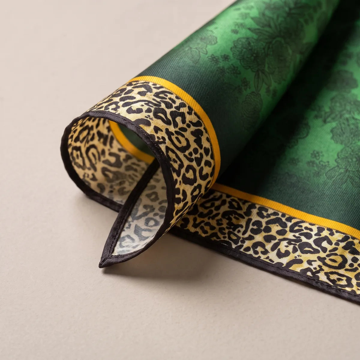 Curled corner of the green scarf showing the leopard border, black edge and pale reverse