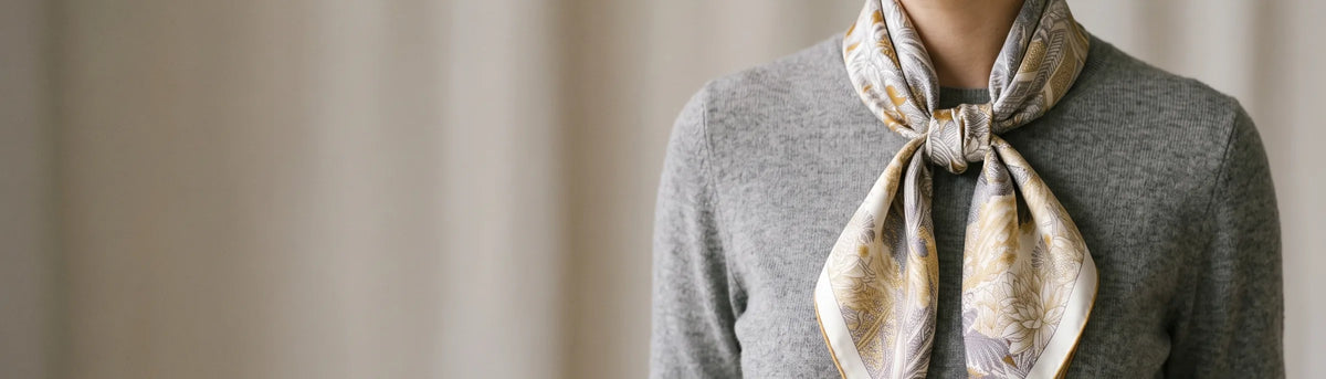 Gray tropical print silk square scarf knotted at the neck over a gray sweater