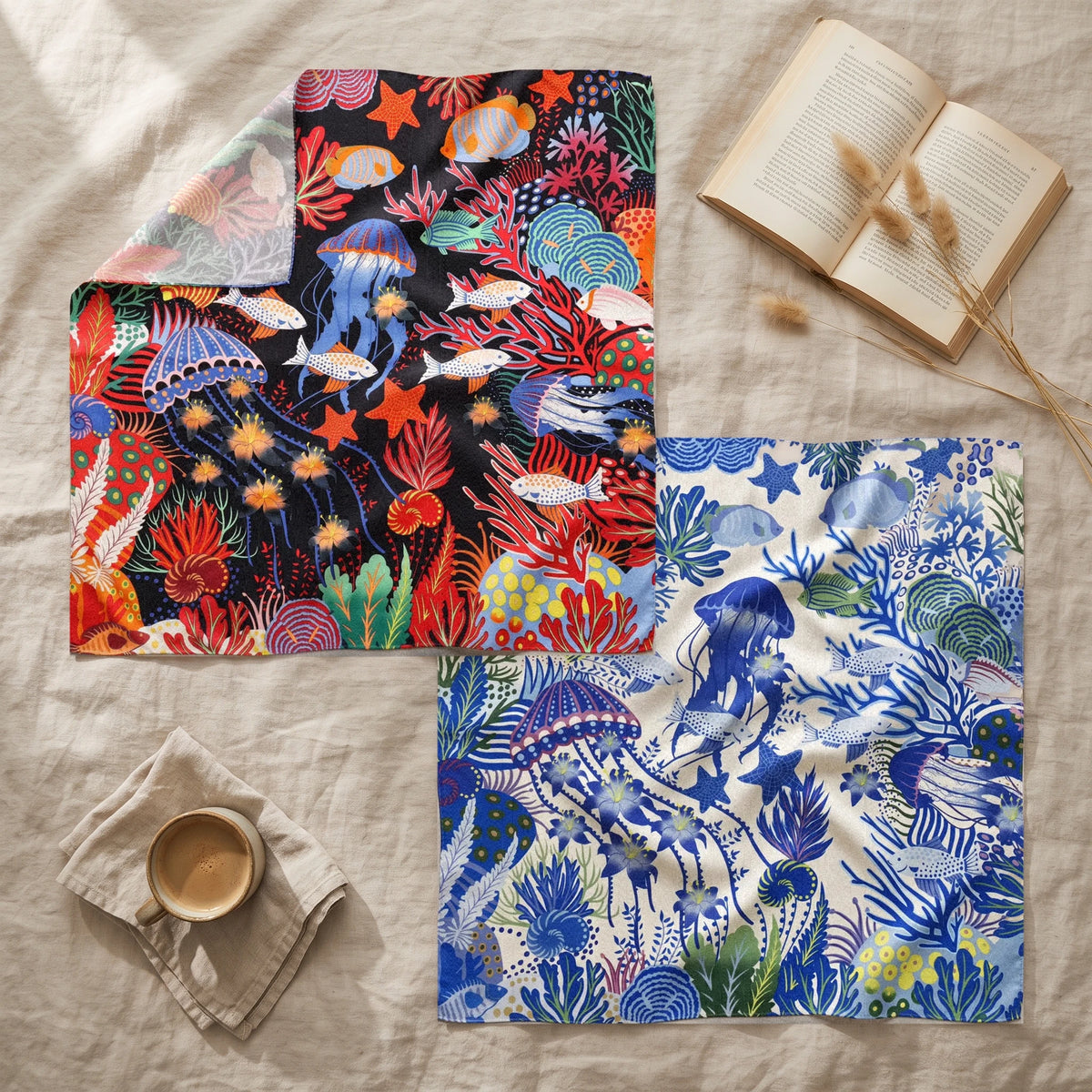 Black and blue jellyfish shawls layered on linen with an open book, a coffee and dried grass