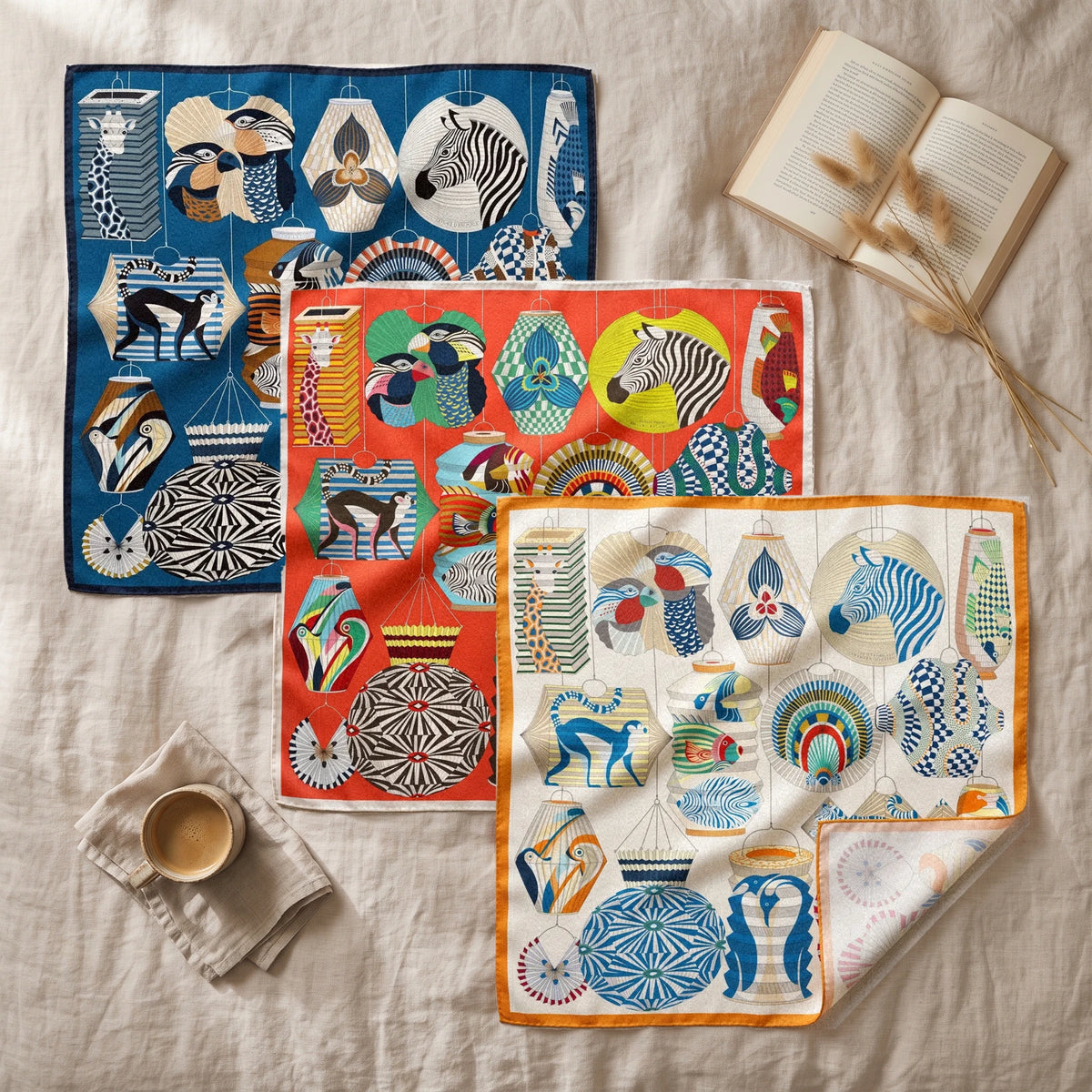 Lantern print squares in blue, red and cream overlapping on linen with an open book and a coffee