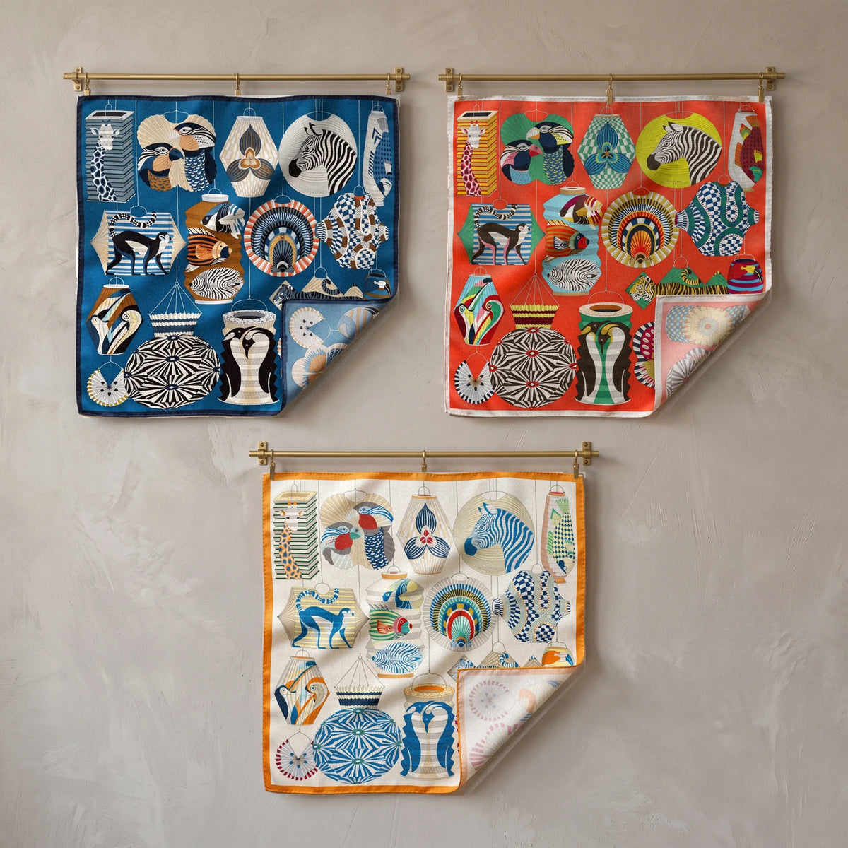 Blue, red and cream lantern print silk square scarves on brass rods, two above and one centered below