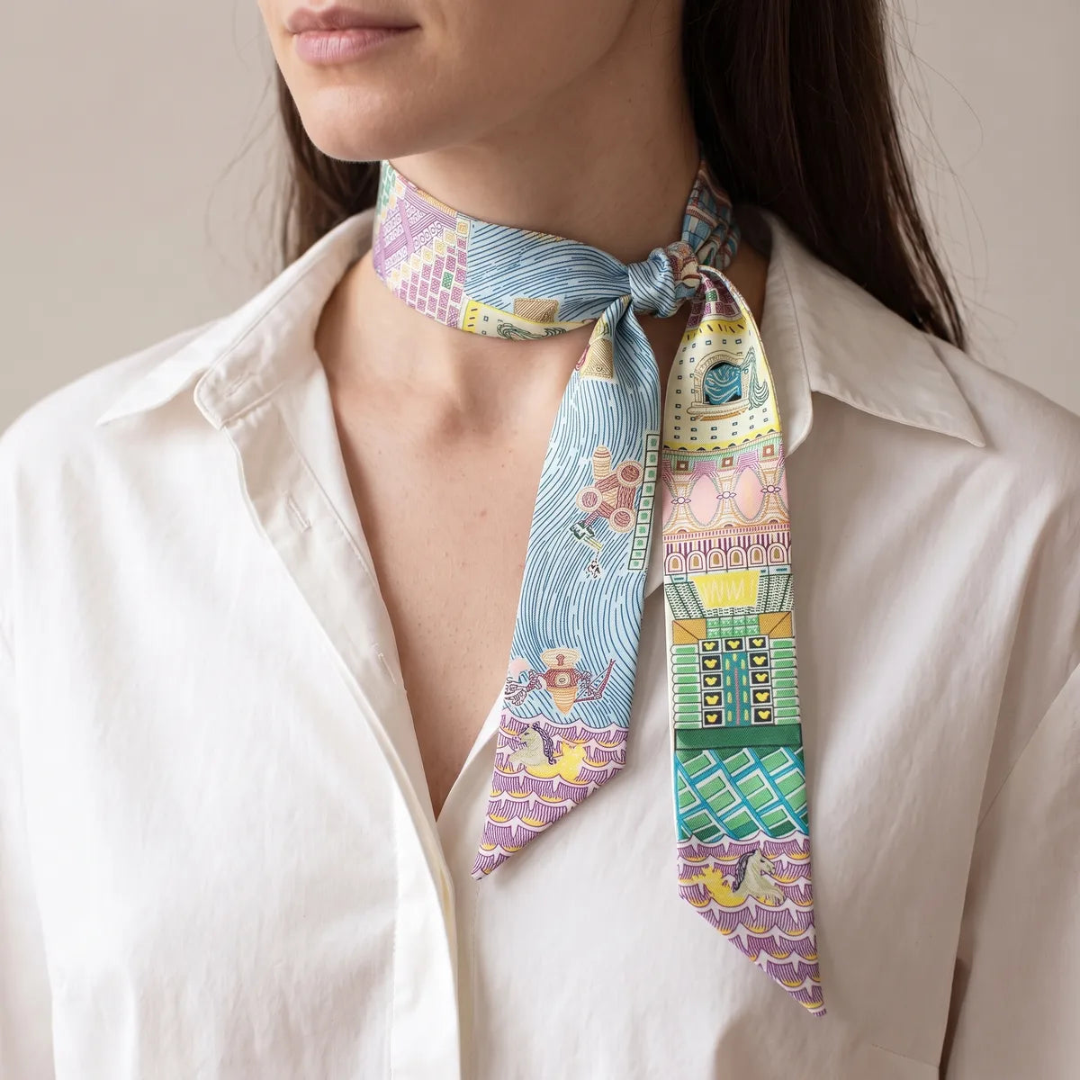 Light blue architecture skinny scarf knotted at the side of the neck against a white collar
