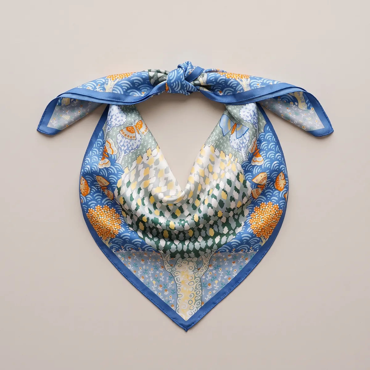 Butterfly silk bandana laid out as a knotted triangle, the dotted green tree at its center, blue waves on both sides