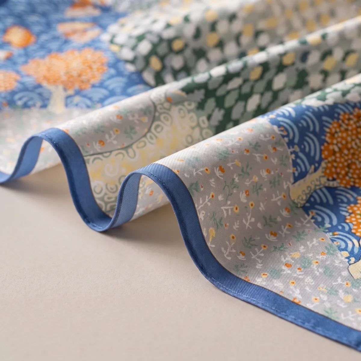 Folds of a butterfly silk scarf with a blue edge: a flowered gray patch, the dotted green tree and blue waves