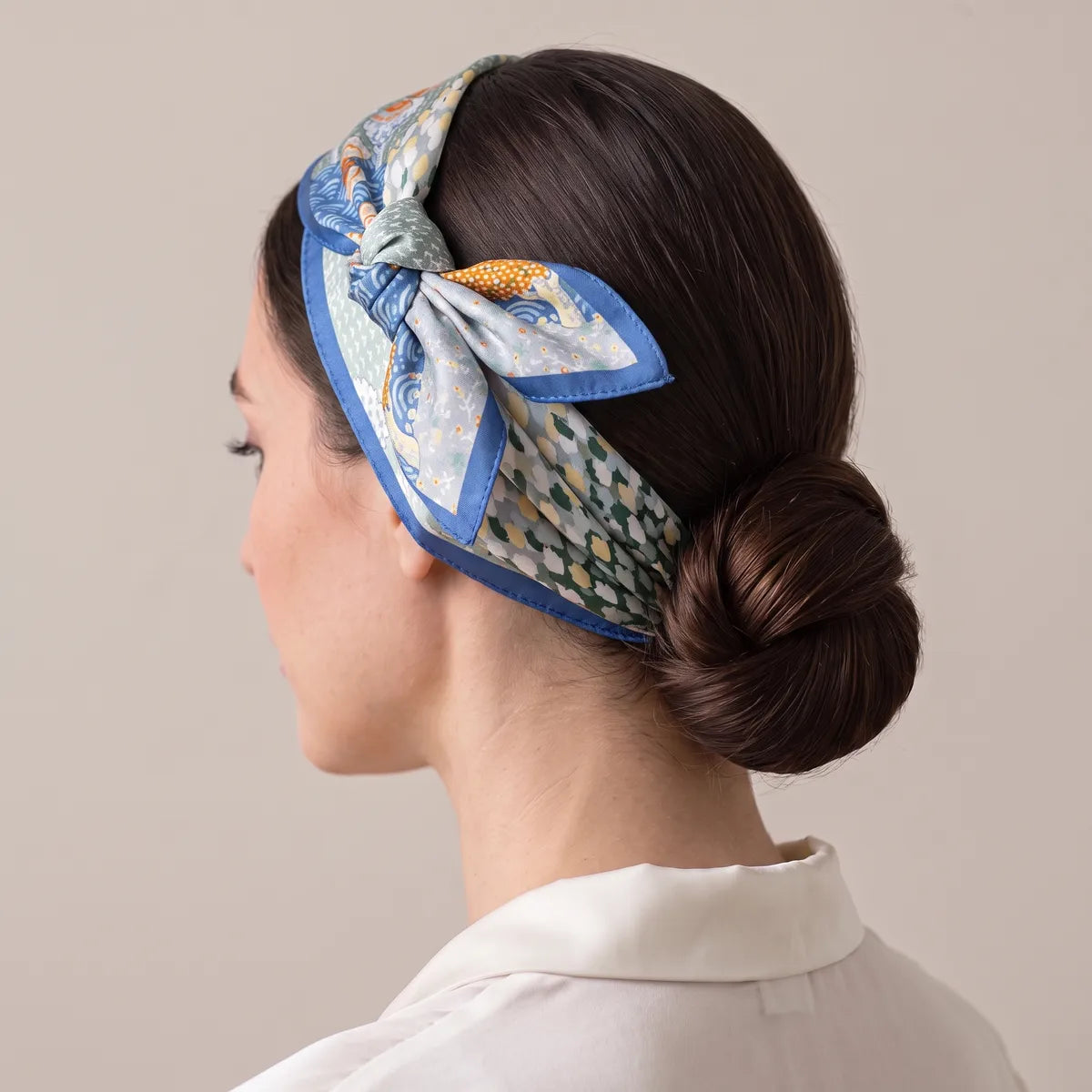 Butterfly print silk scarf in light blue banding the hair, tied off above the ear, low bun at the nape