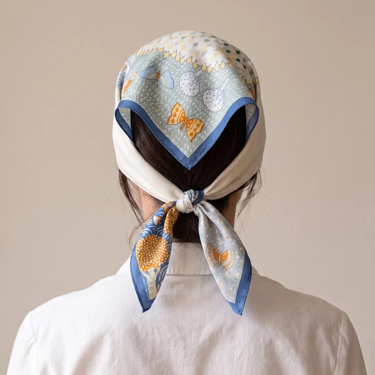 Light blue silk bandana worn as a kerchief over the hair, knotted at the nape with an orange butterfly on the tail