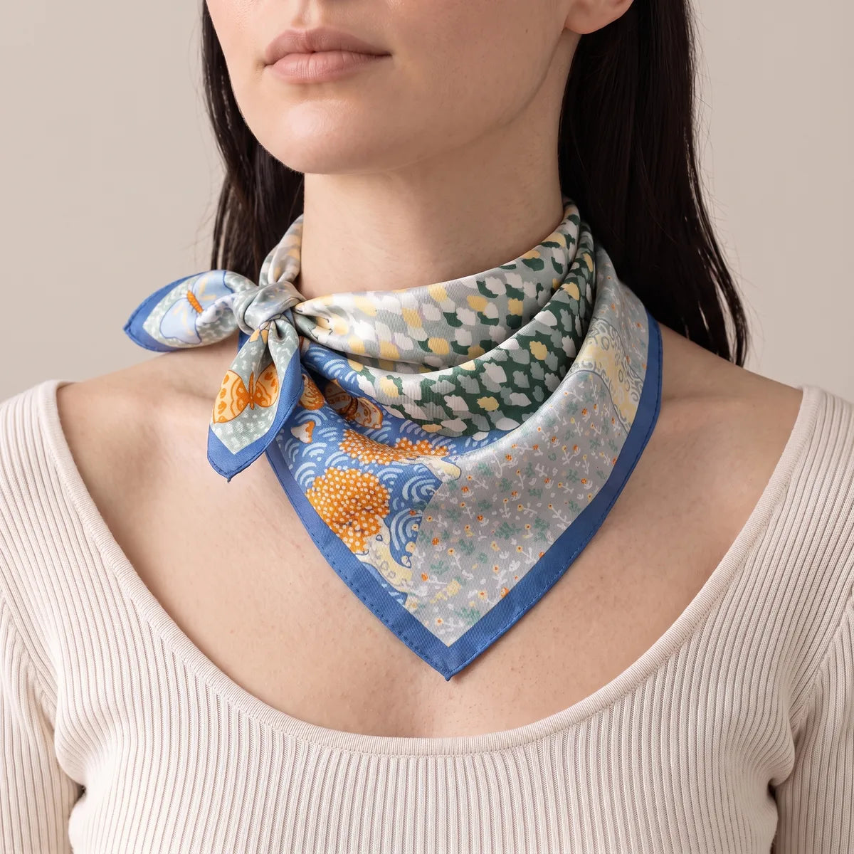 Light blue butterfly silk bandana knotted to one side over a cream ribbed top, orange trees and waves in front