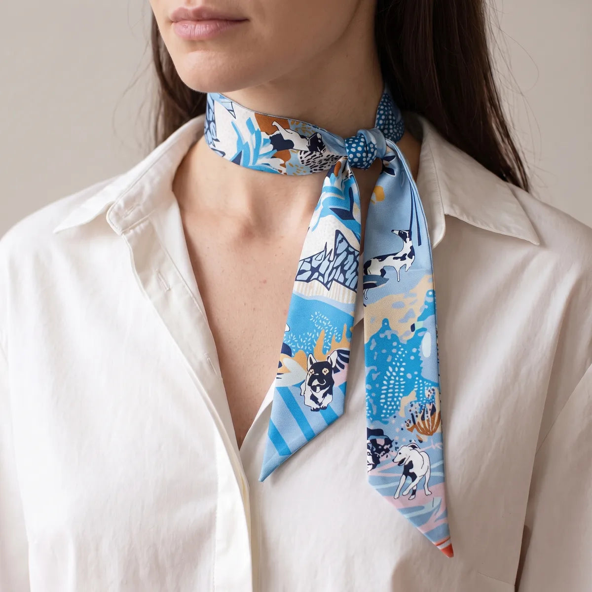 Light blue dog print skinny scarf with a side knot at the neck, ends falling over a white shirt