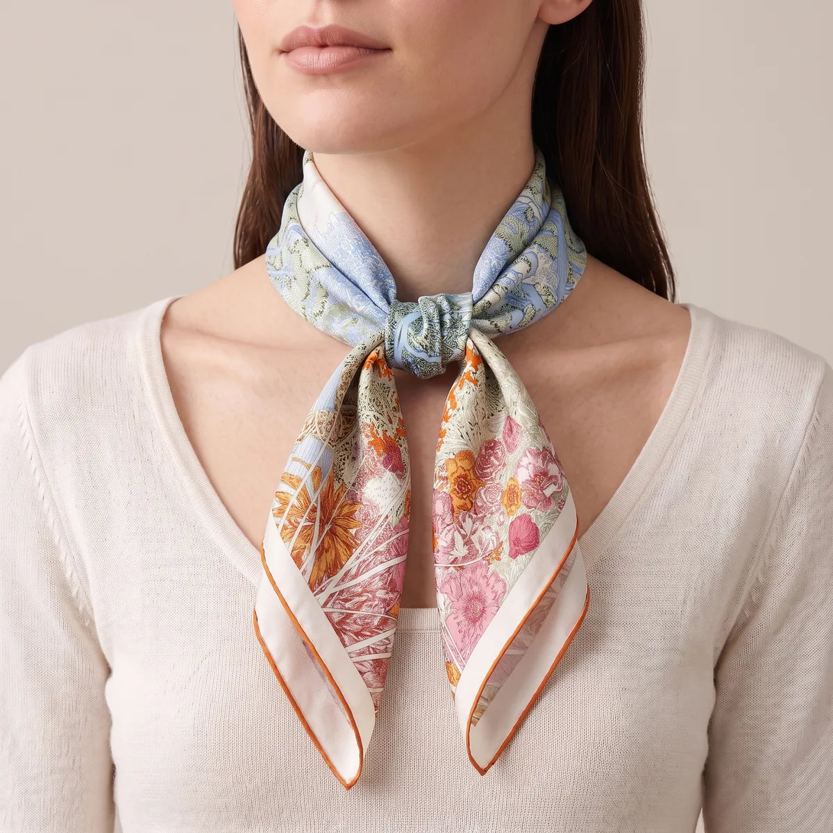 Woman in a cream sweater with the pastel garden square knotted at the front of her throat