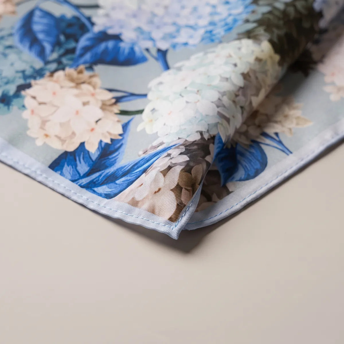 Close-up corner of the hydrangea bandana: cobalt leaves, white florets and the narrow light blue edge