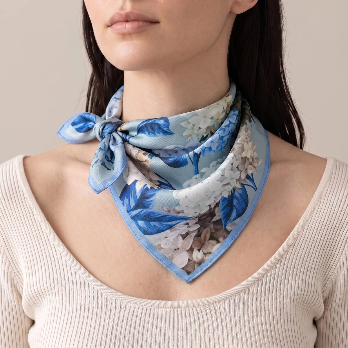 Light blue floral silk scarf on a woman's neck, knotted off to the side above a cream ribbed top