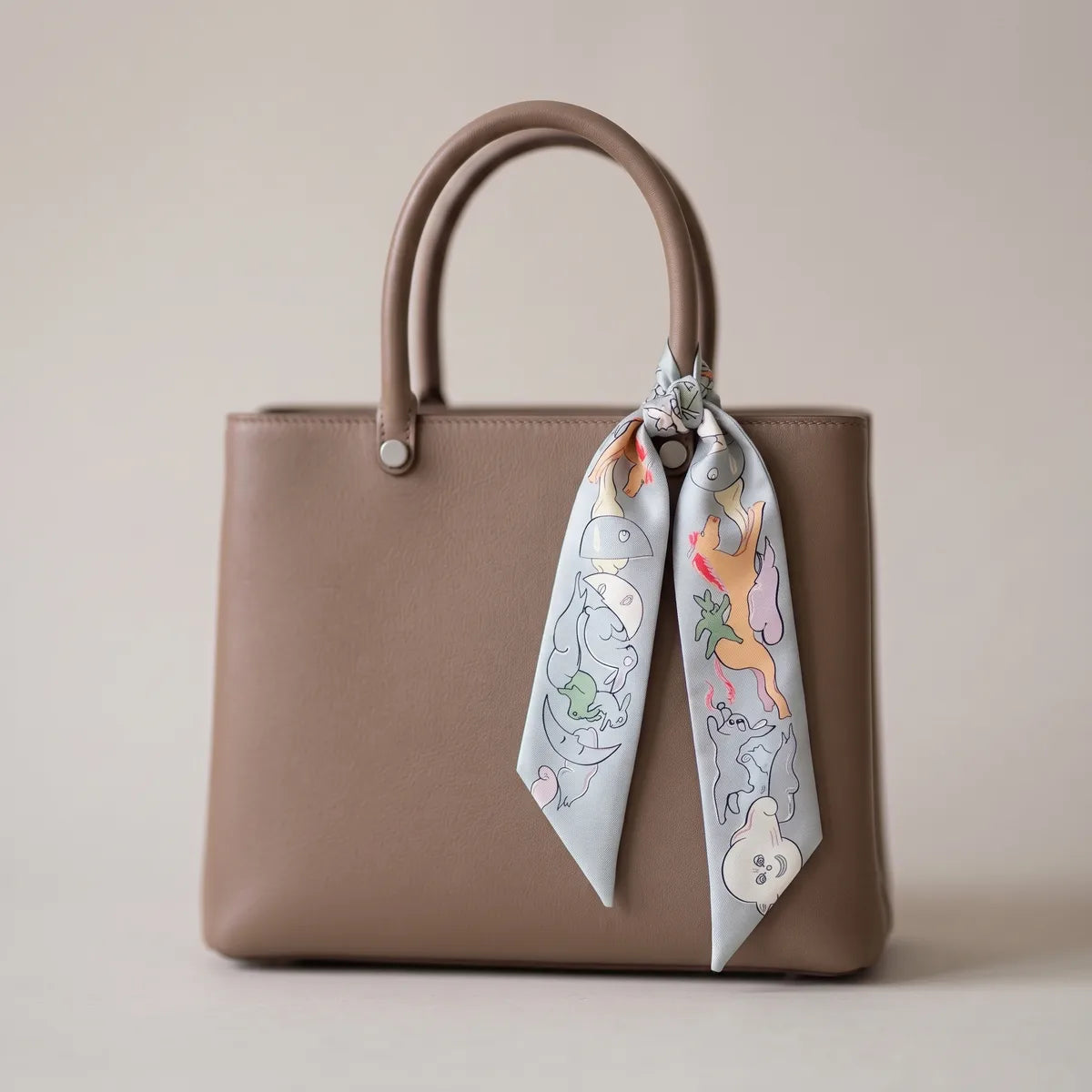 Light blue moon print skinny silk scarf hanging from the handle of a taupe bag