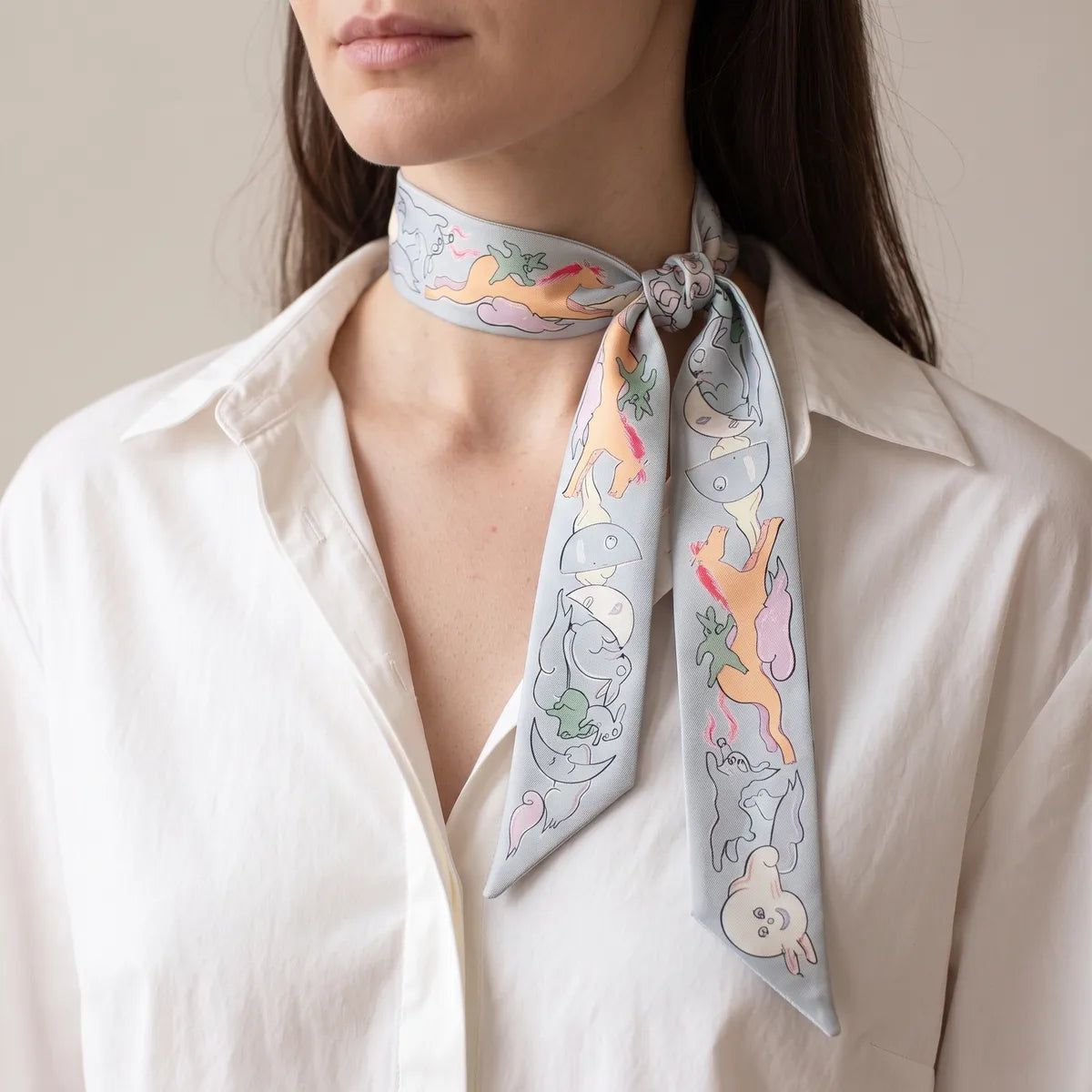Light blue moon print skinny scarf tied to one side of the neck, worn with a white shirt