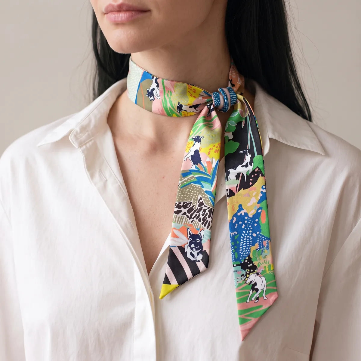 Multicolor dog print skinny scarf knotted near the side of the neck, striped tip hanging in front