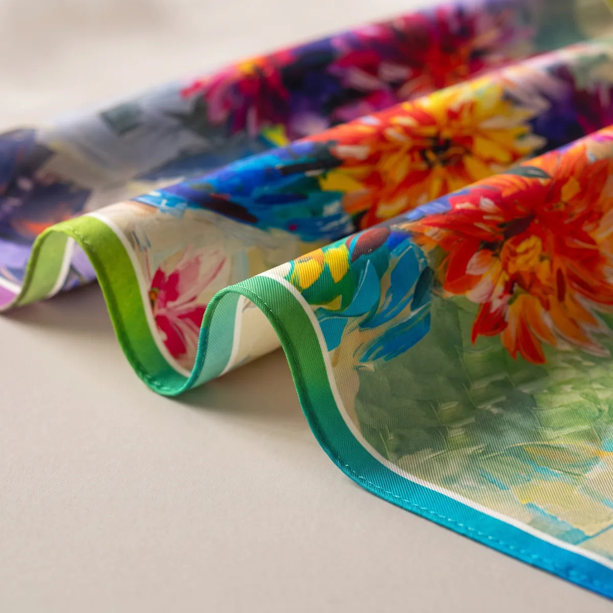 Green and turquoise edge of a floral silk bandana, orange and yellow blooms curving over the folds