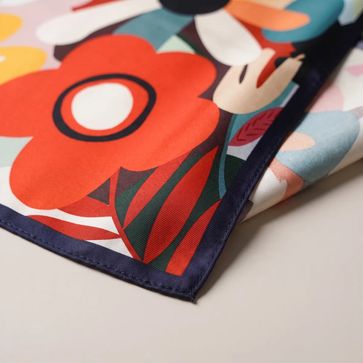 Corner of the multicolor bandana: red-orange petals, green leaves and the thin navy hem