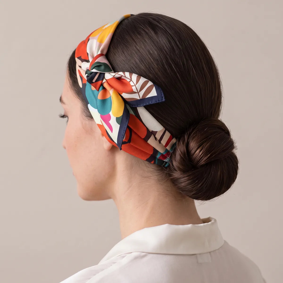 Bright floral bandana wrapped as a headband, knot high above one ear, dark hair in a bun
