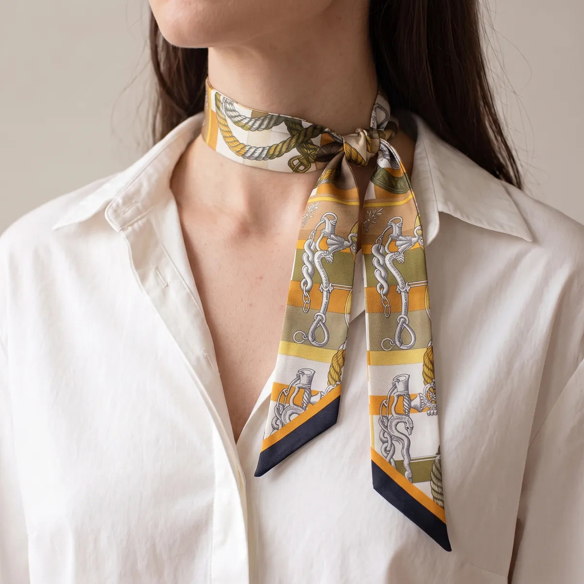 Mustard chain print skinny scarf knotted to the side at the neck, navy tips hanging