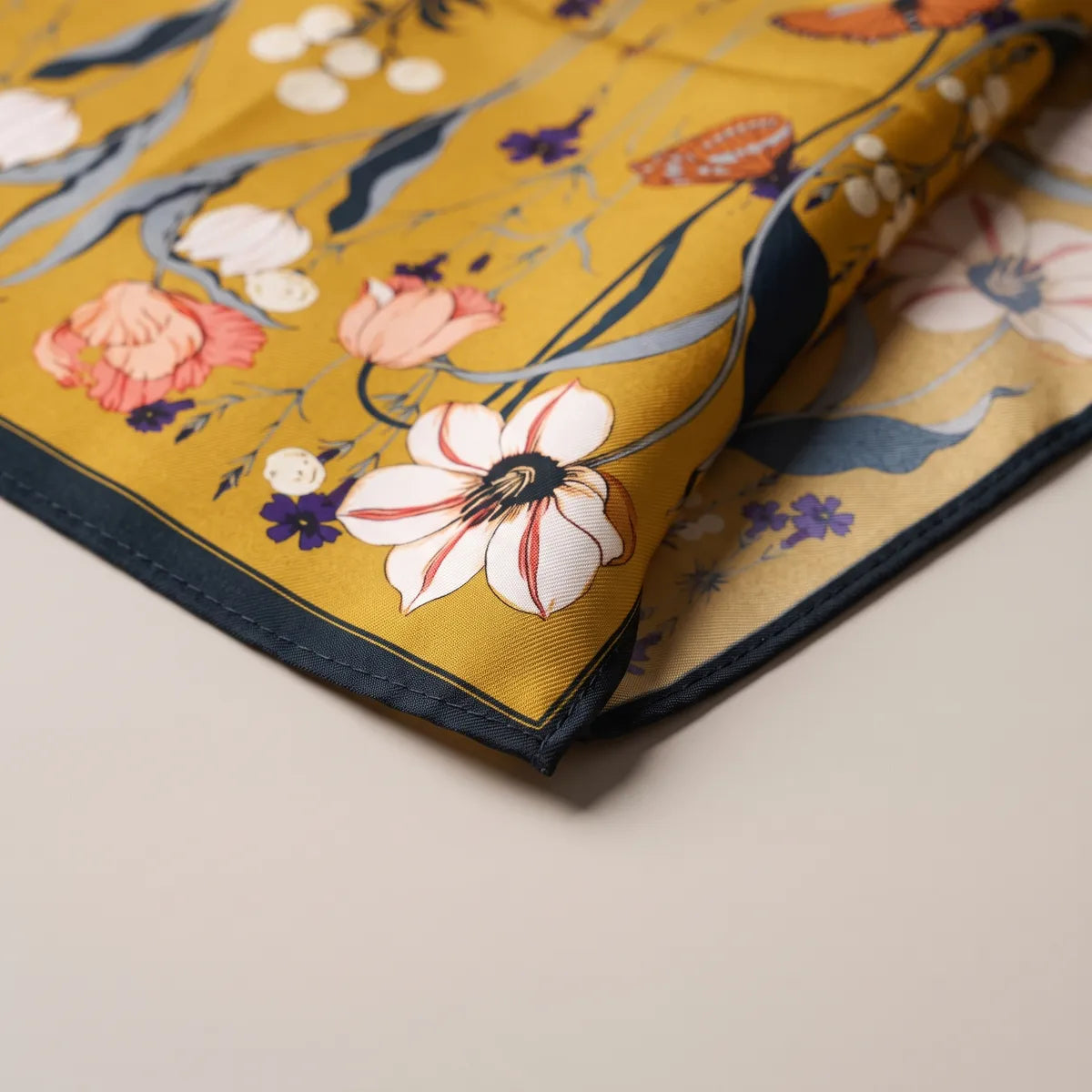 Corner of the mustard floral bandana with coral tulips, violet florets and the navy edge