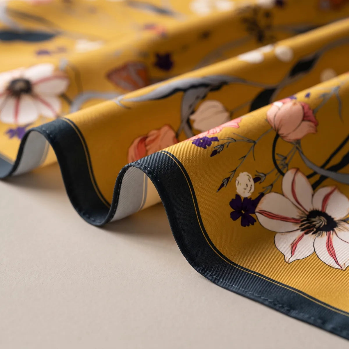 Close view of the mustard bandana draped in waves, navy hem and a red-streaked white lily