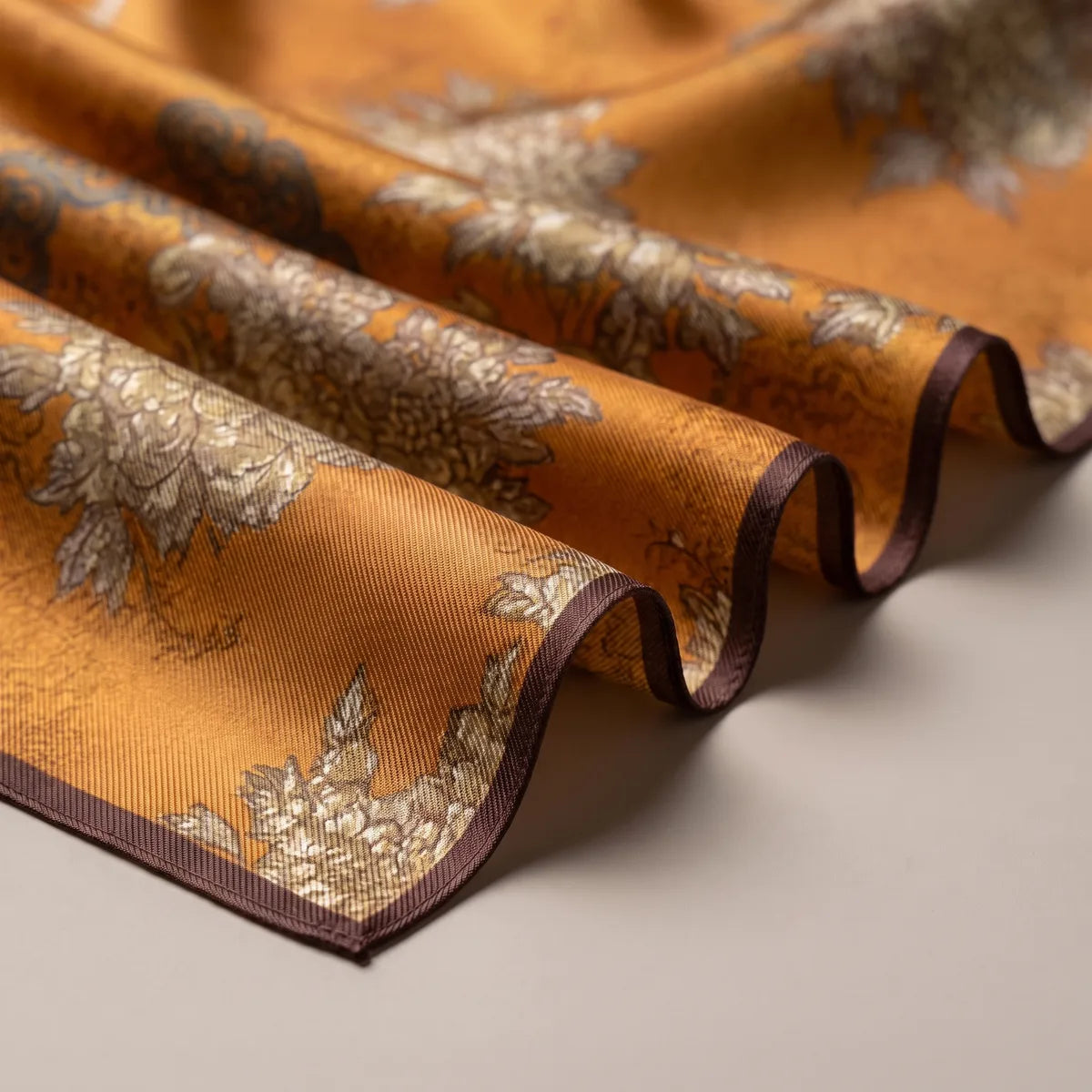 Folds of mustard silk showing beige flower heads and a narrow chocolate-brown hem