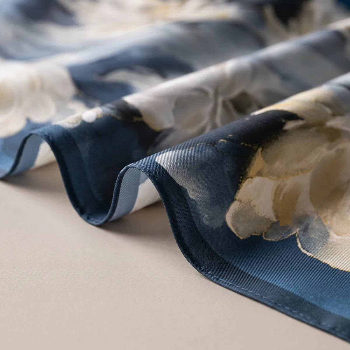 Wavy folds of the navy floral bandana showing its plain navy edge and a cream bloom in close-up