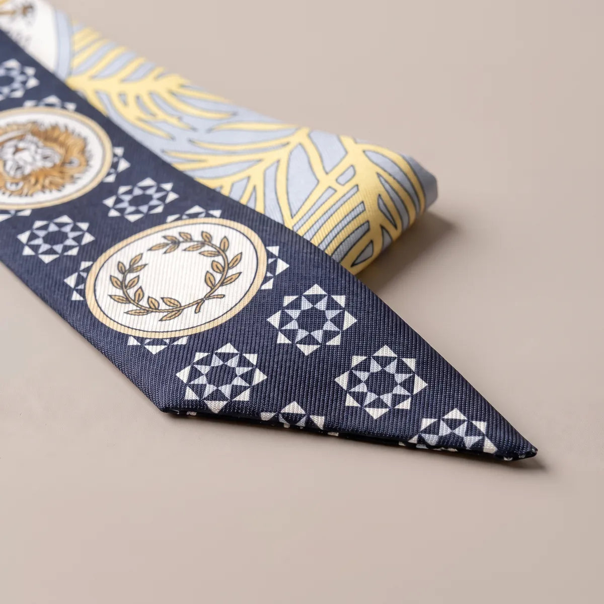 Navy skinny scarf tip folded over: a laurel wreath medallion among white star tiles, leaves behind