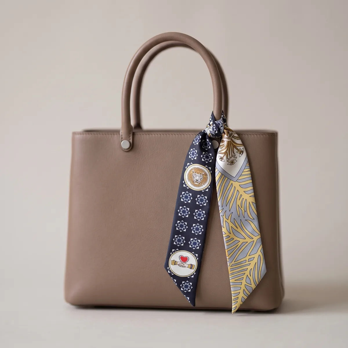 Navy medallion print skinny silk scarf hanging from a taupe leather bag handle