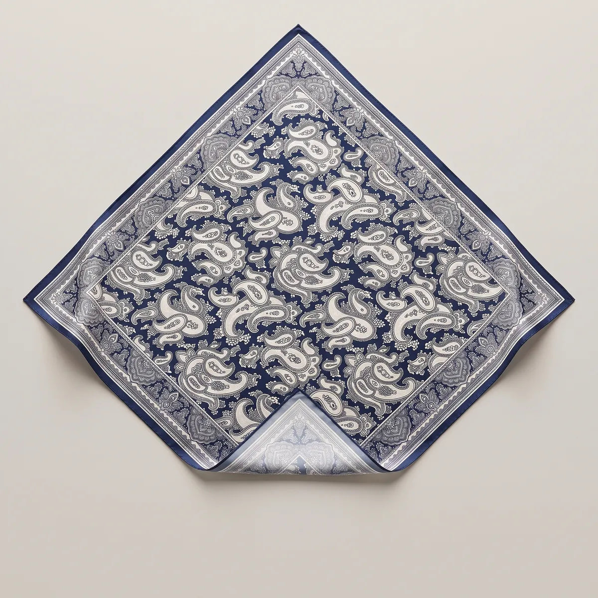 Navy paisley silk bandana laid flat, ivory paisleys on deep navy in a lace-like border, a corner folded to the pale reverse
