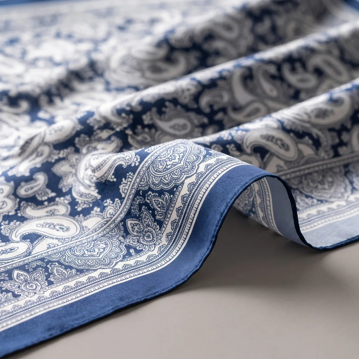 Close-up of the navy edge and ivory paisley border on a silk bandana, the fabric draped in folds