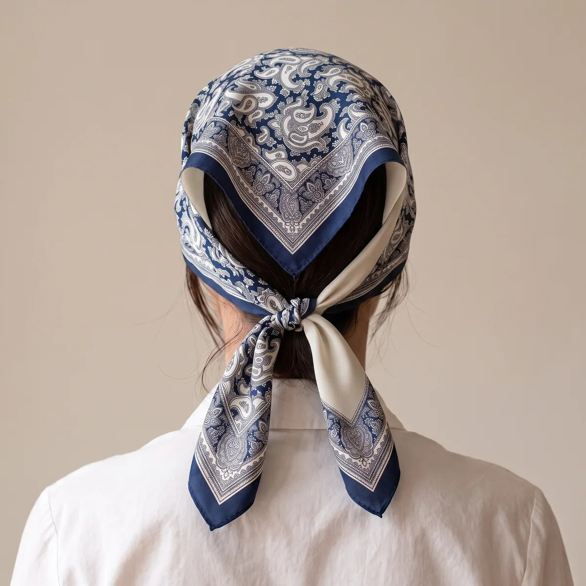 Navy paisley kerchief seen from the back, its ends knotted at the nape on top of the gathered hair