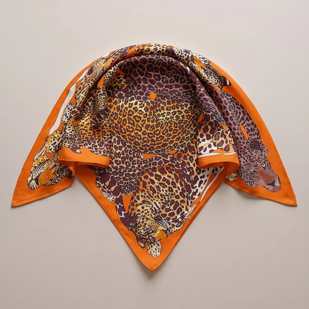 Leopard print silk shawl folded into a triangle, spotted coats in tawny and brown framed by bright orange