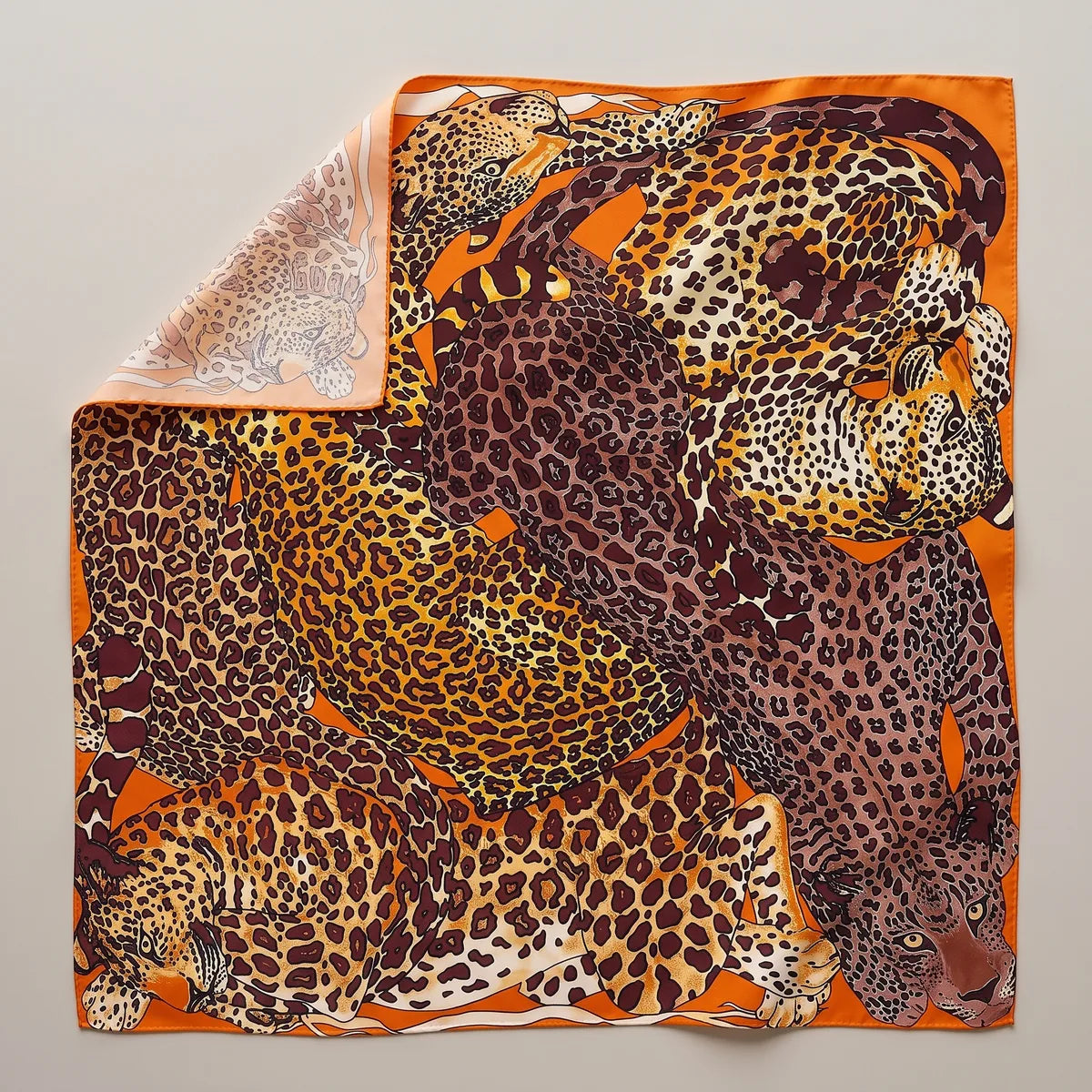 Orange and brown leopard print silk shawl laid flat: tawny and plum-brown leopards piled up, orange border, corner folded