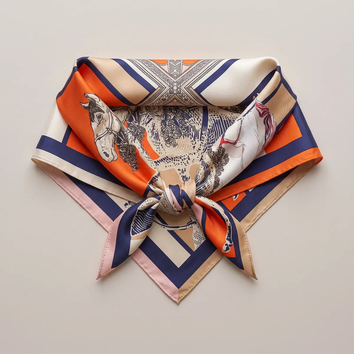 Horse print silk square knotted into a triangle and laid flat, a pale geometric panel above the knot