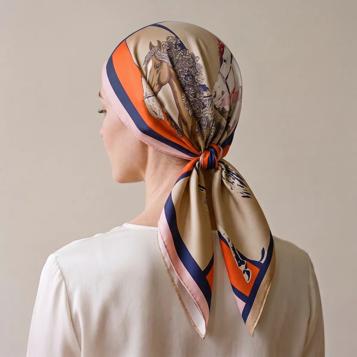 Orange, navy and pink horse print silk square worn over the hair and knotted at the nape