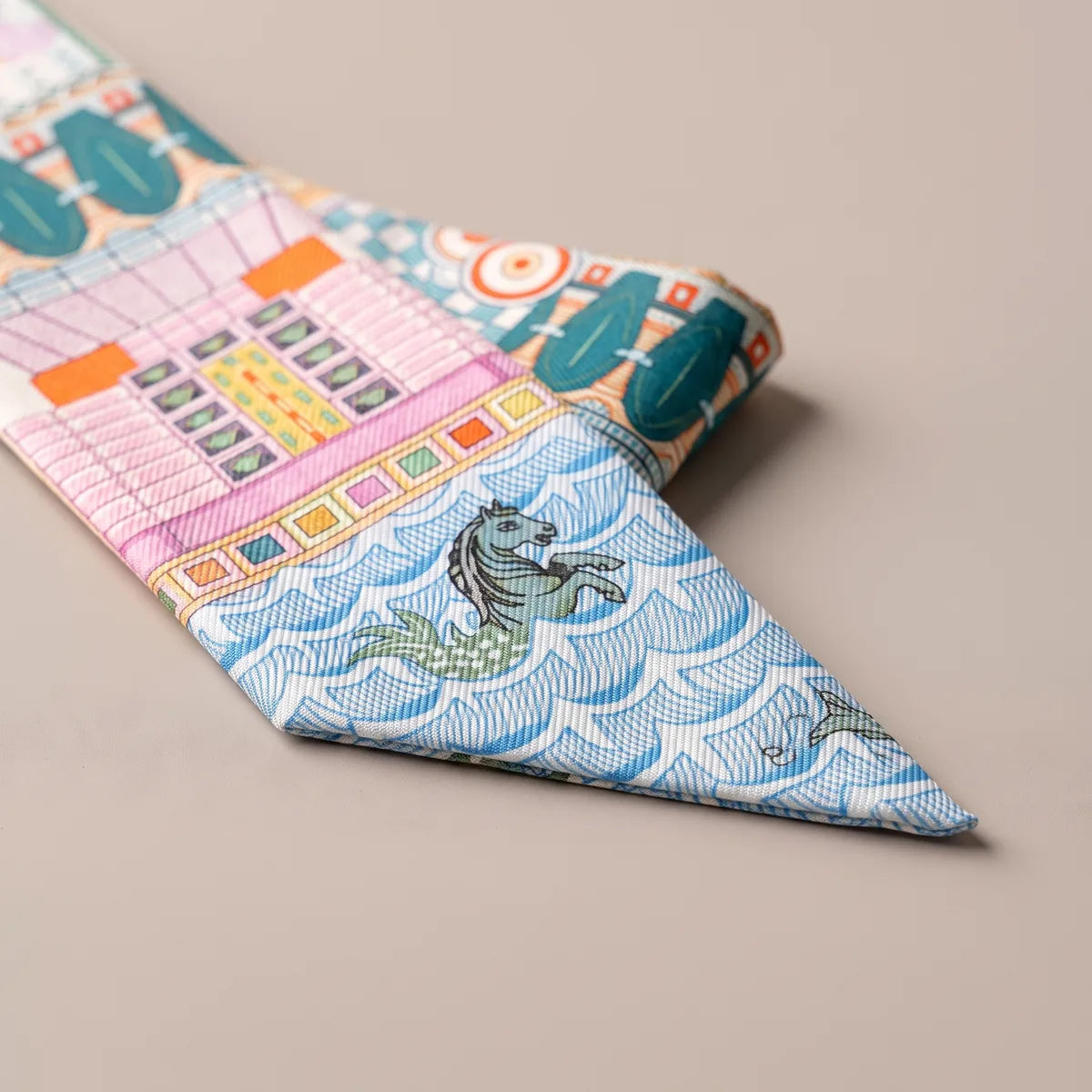 Close-up of the orange skinny scarf's blue scalloped tip with a dark gray seahorse below pink facades