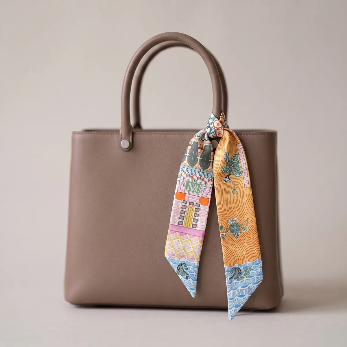 Orange architecture skinny silk and satin scarf tied to a taupe bag handle, the orange strand hanging