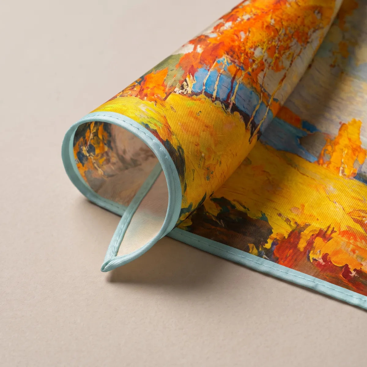 Turned-up corner of the autumn scarf showing orange foliage, a yellow field and the aqua edge